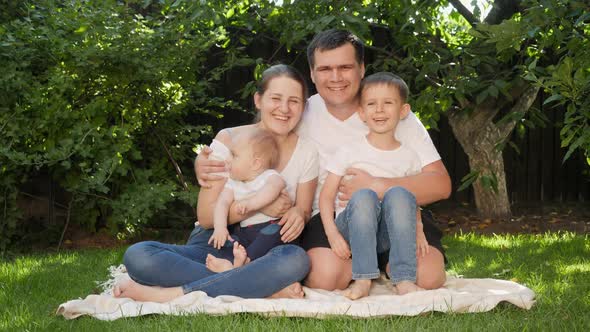 Happy Smiling Parents with Two Sons Sitting on Grass in Park and Having Good Time Together