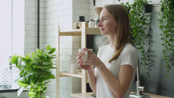 Young Happy Woman Drinks Coffee in the Kitchen in the Morning at Home