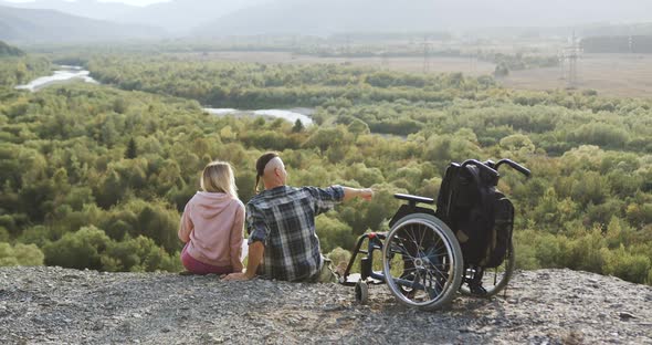 Couple which Sitting Together Near Man's Wheelchair on the Top of the Mount and Talking