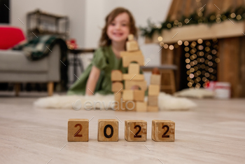 Wooden cubes with the numbers 2022 stand on the floor in a row. Background of a blurred happy girl