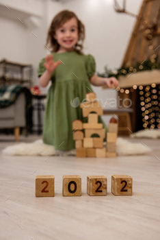 Wooden cubes with the numbers 2022 stand on the floor in a row. Background of a blurred happy girl