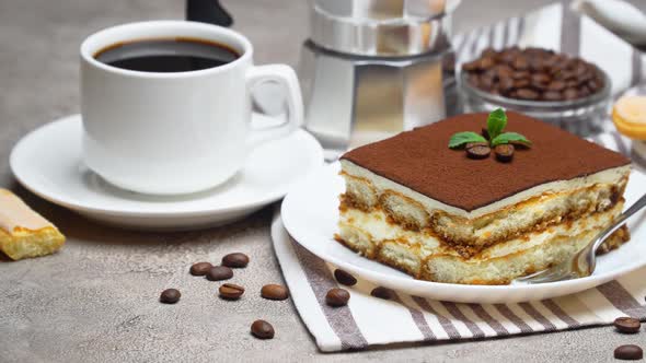 Portion of Traditional Italian Tiramisu dessert and cup of coffee on grey concrete background