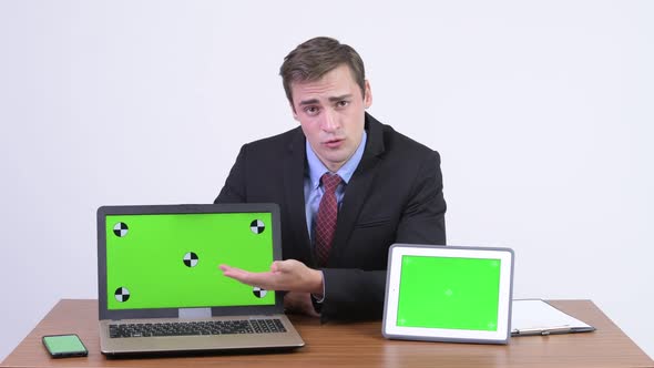 Young Handsome Businessman Presenting Something on Laptop and Digital Tablet Against Wooden Table