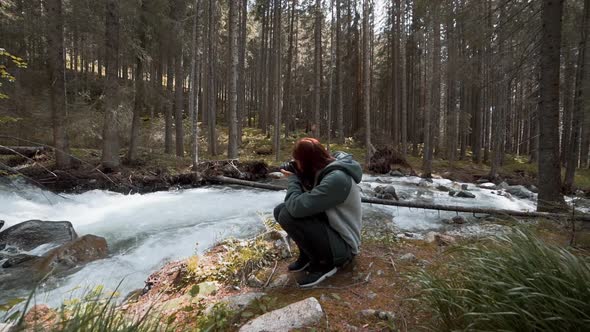 Happy Young Redhaired Woman Photographs a Mountain Forest and a River in the Dolomites Mountains