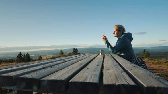A Woman Sits at a Table Uses Her Phone High in the Mountains of Norway