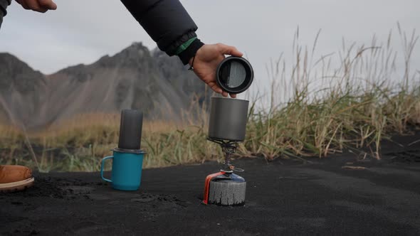 Man Removing Lid From Cup On Camp Stove On Beach