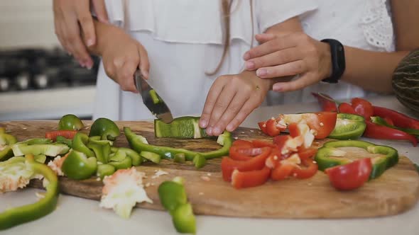 Mother Teaching Her Daughter Cutting vVegetables at Home in Kitchen.