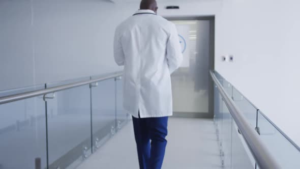 Back view of african american male doctor walking through hospital corridor