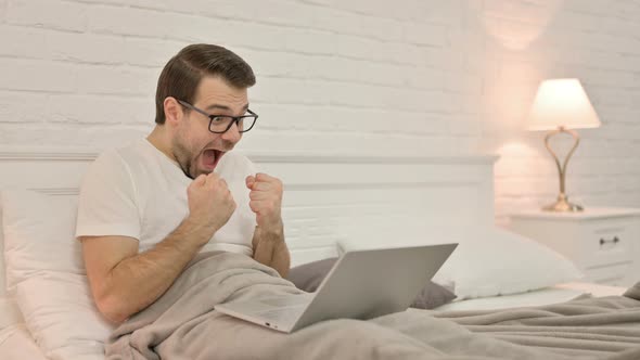 Excited Young Man Celebrating on Laptop in Bed