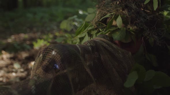 Sniper Looking Through Scope of Optical Sight Taking Aim in Forest