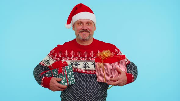 Cheerful Man in Santa Sweater Presenting Two Christmas Gift Boxes Stretches Out His Hands to Camera