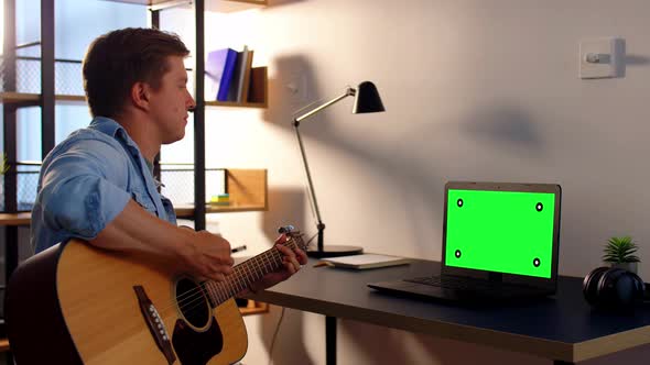 Young Man with Laptop Playing Guitar at Home