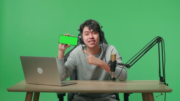 A Smiling Asian Man With Computer Reviewing Camera Len While Sitting In Front Of Green Screen