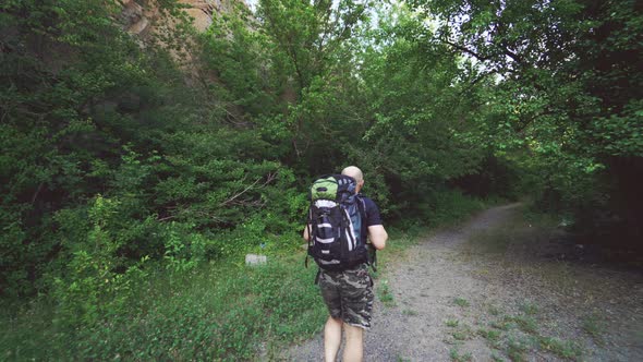 Tourist With a Backpack in Shorts and a Shirt is Going Along a Path in the Forest