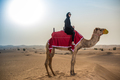 Young woman wearing traditional middle eastern clothes riding camel in desert, Dubai, United Arab - PhotoDune Item for Sale