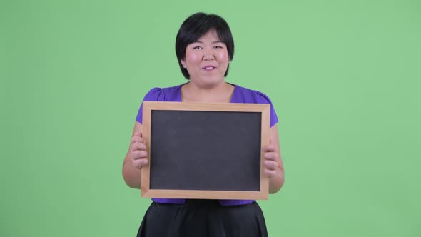 Happy Young Overweight Asian Woman Holding Blackboard and Looking Surprised