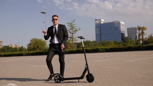 A Happy Businessman Is Dancing in a City Park Next To an Electric Scooter