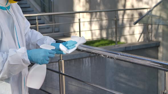 A Young Sanitary Worker Wearing a Protective Suit and a Respirator Cleans and Disinfects the