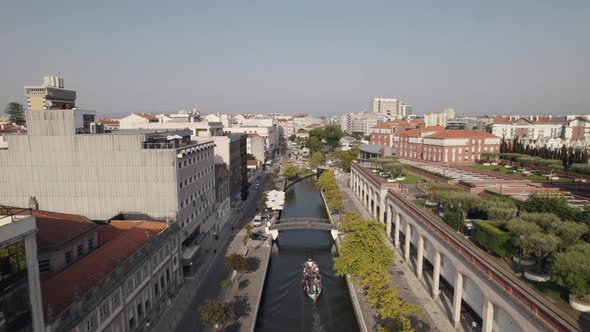 Aerial descending shot of moliceiro boat cruising on water canal under pedestrian bridge.