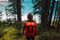 High angle rear view of mid adult woman carrying orange colour backpack standing in forest looking - PhotoDune Item for Sale