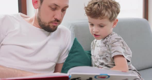 Close Up of Father and Son are Spending Time Together at Home By Reading a Book on the Sofa and