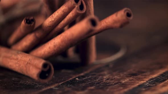 A Super Slow Motion Pile of Cinnamon Sticks Falls on a Wooden Table