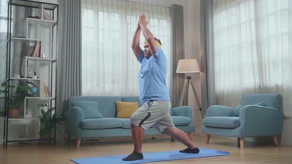 Fat Asian Man Doing Yoga In Warrior I Pose On Mat  At Home