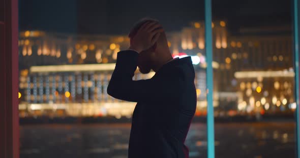 Young Businessman Standing Depressed Near Window in Office at Night