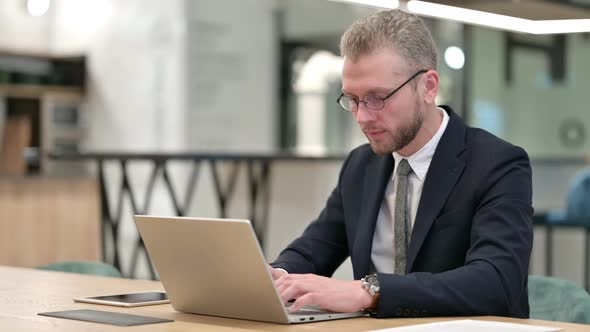 Thumbs Down By Serious Young Businessman with Laptop in Office