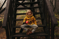Blonde Child in Yellow Coat Sitting on Wooden Stairs Outdoors and Drinking Tee From a Travel Cup - PhotoDune Item for Sale