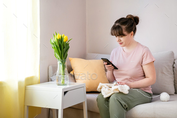 Young woman knitting white knitwear and holding mobile phone