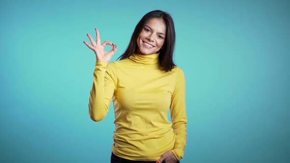 Young woman making OK sign over blue background. Winner. Success. Positive brunette