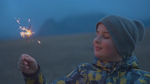 A Boy with a Bengali Fire in His Hand Stands in the Evening Outdoors