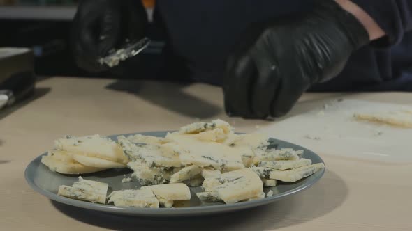 Pastry Chef with a Large Knife Cut Cheese with Mold Dorblu Into a Bowl