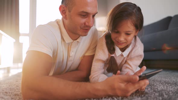 Father and Daughter Enjoying Time Together and Using a Tablet for Family Entertainment While Lying