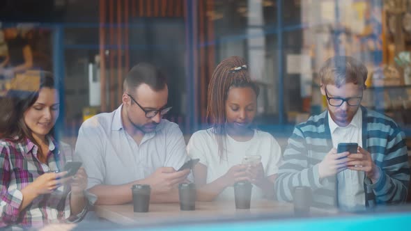 Four Diverse Friends Sitting in Coffee Shop Using Smartphones Ignoring Each Other