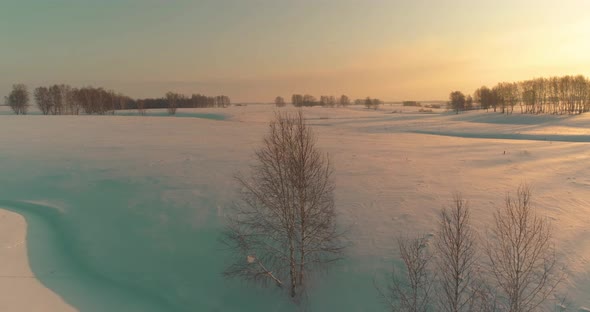 Aerial View of Cold Arctic Field Landscape Trees with Frost Snow Ice River and Sun Rays Over Horizon