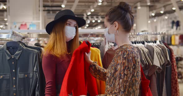 Two Lovely Young Women in Safety Mask Chatting While Shopping Together for New Clothes