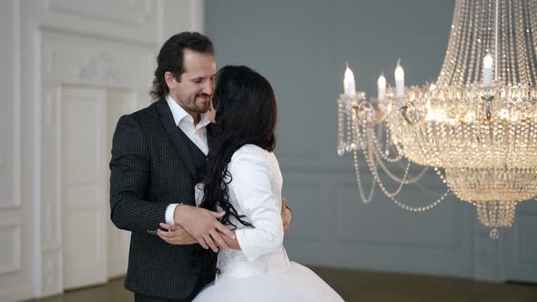 the Bride Approaches the Groom on the Background of a Crystal Chandelier