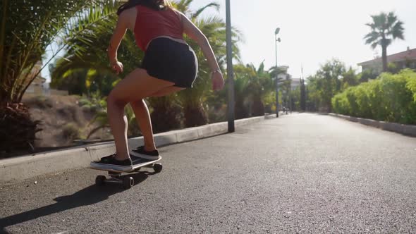 Girl on a Skateboard in Short Shorts Rides on the Road Along the Beach and Palm Trees