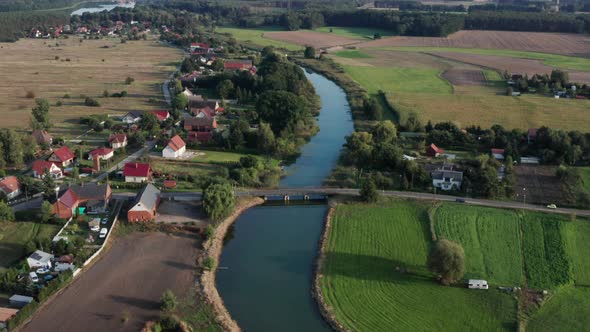 Aerial rural shot of a small village and farms by the river. Camera tilts down to focus on a wooden