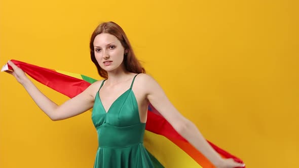 Young Beautiful Woman of Caucasian Ethnicity Cute Smiling with LGBT Flag on Yellow Pastel Background