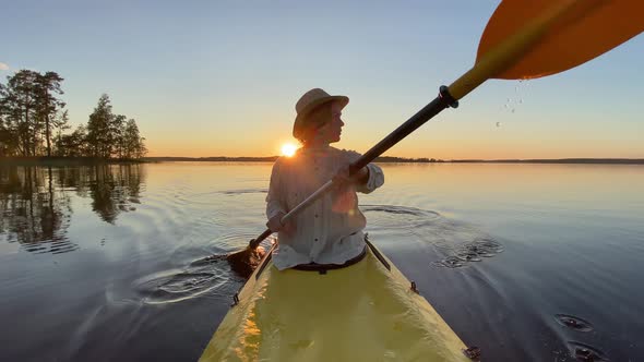 Young Man in a Straw Hat and Linen Shirt is Sailing on a Yellow Kayak on a Calm Forest Lake at