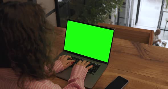 High angle shot of businesswoman texting with colleagues via laptop with green screen.