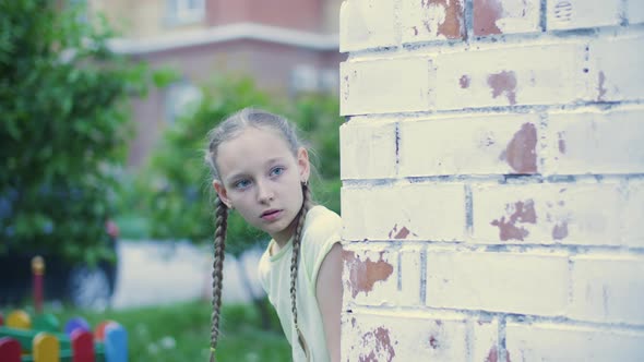 Scared Girl Teenager Peeping Out From Brick House Corner in Residential District. Worried Girl