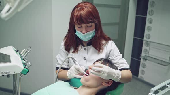 Female patient lying in dental couch and dentist in medical clothes cleaning her teeth with brush.