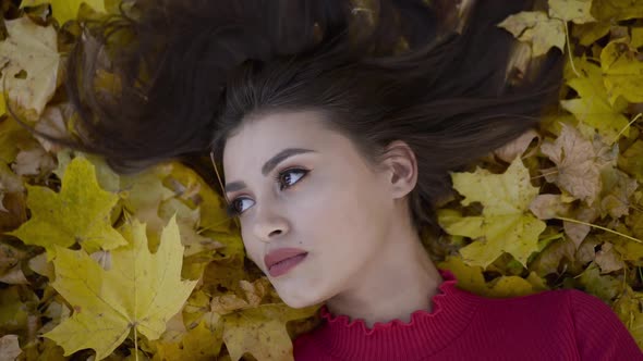 Close Portrait of Beautiful Girl Lying on Autumn Leaves and Looking Into Camera