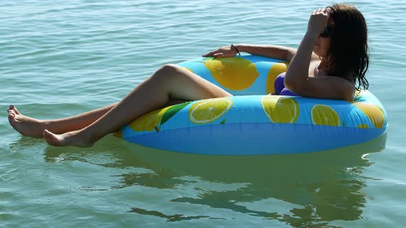 Young woman lying on an inflatable mattress with lemons, floating and relaxing in the sea.