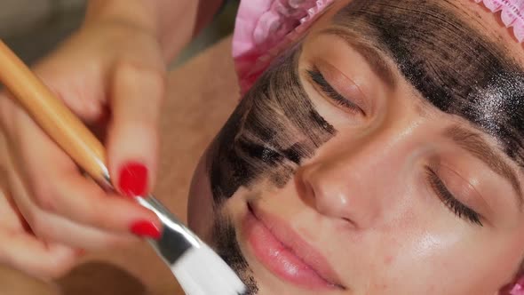 Woman Having Black Facial Mask Being Applied on Her Face By Cosmetologist