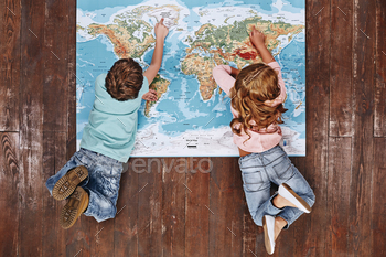 boy and girl on vintage brown wooden floor. Children lying on world map, looking at it
